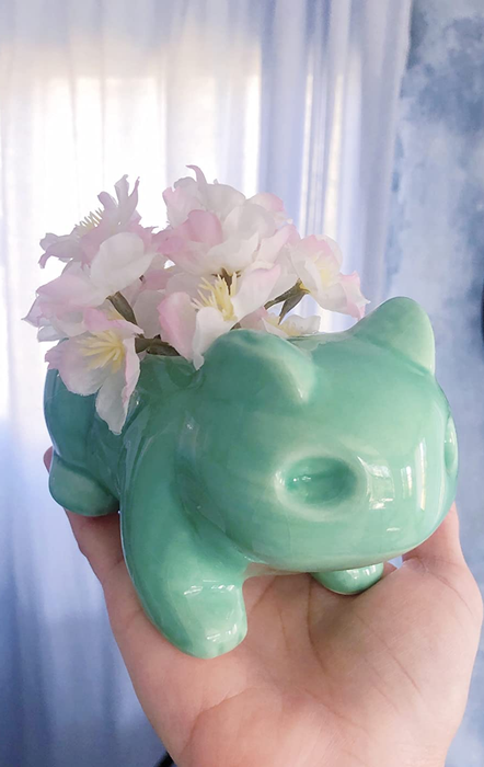 A hand holding the Bulbasaur planter filled with pink flowers.