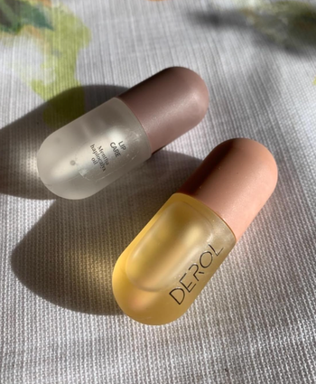 A pair of lip balm tubes with clear caps, one marked with a label.