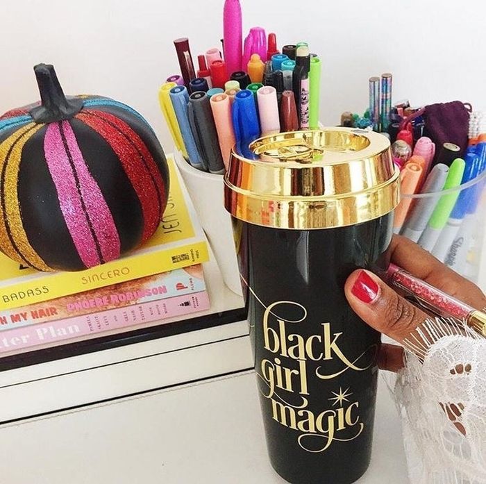 A model holding a black travel mug with a gold lid and the gold-inscribed words