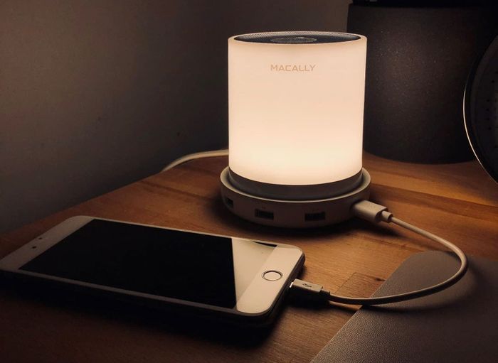 A bedside light with a cellphone charging next to it.