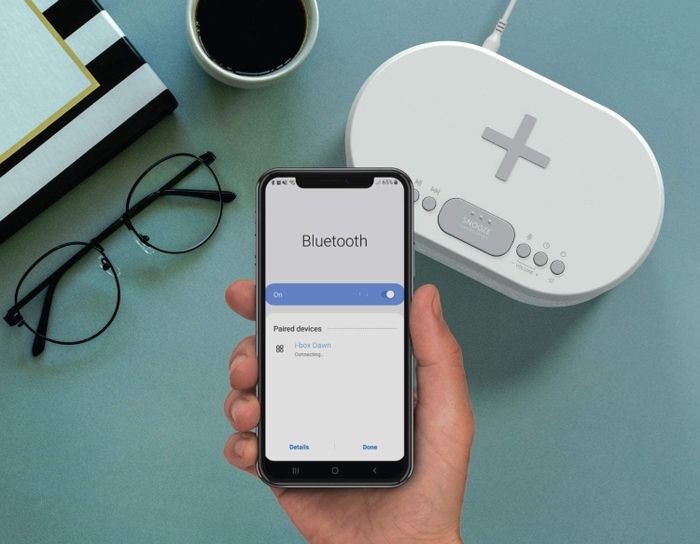 A person holding their smartphone close to the alarm clock.