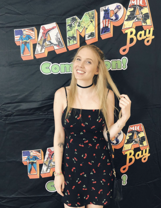 A reviewer wearing a black spaghetti strap mini dress with a cherry print