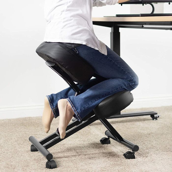 A person resting their knees on a support bar and sitting on a low chair with their bottom on a pad.