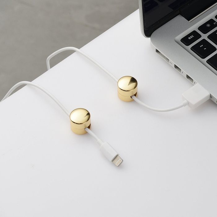 A set of two gold-finished round cable organizers attached to a desk, with a charger wire running through them.