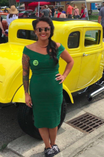 A reviewer posing in the green dress in front of a vintage car