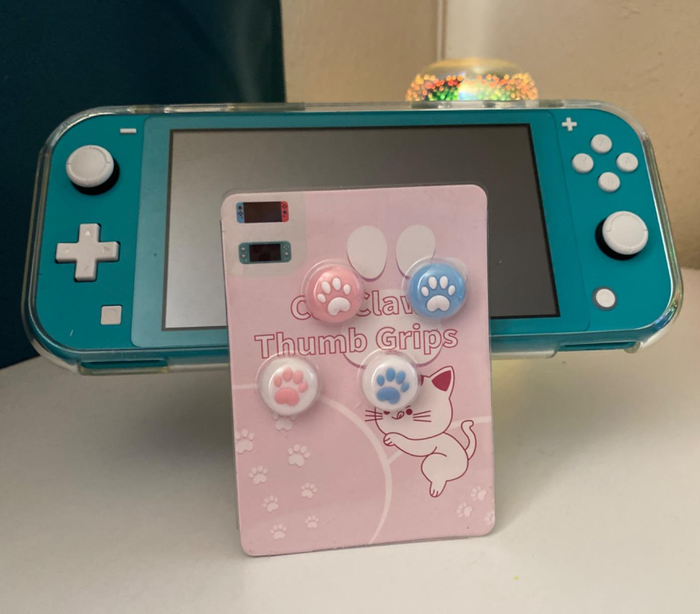 A reviewer shows their Nintendo Switch alongside the package containing four paw print joystick caps, demonstrating how these small accessories can elevate the look of the console.