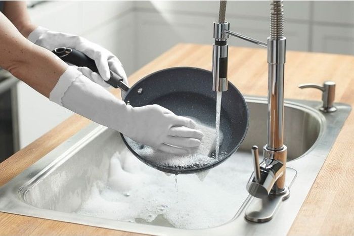 A hand wearing gloves scrubbing a pan clean.