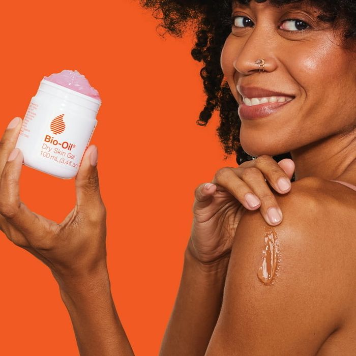 A model applying the product to her skin, set against an orange background