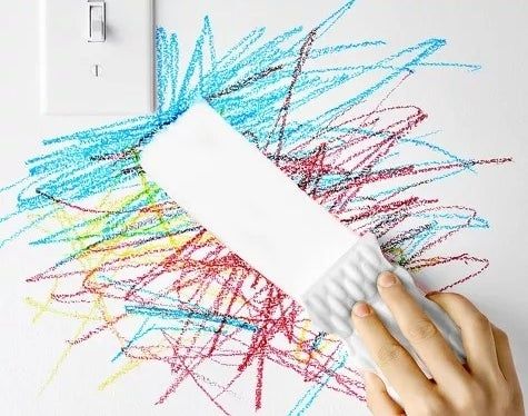A magic eraser effortlessly removes crayon marks from a wall.