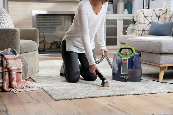 A person uses a portable deep cleaning vacuum on a rug.