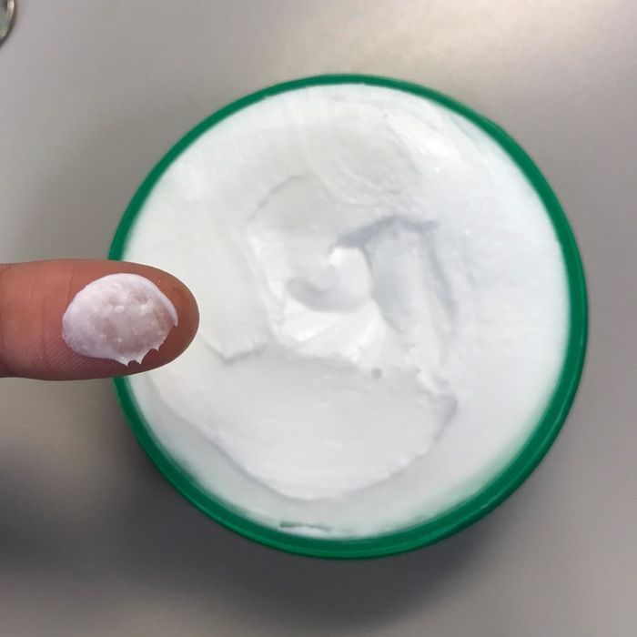 A photo featuring the jar of the hand cream with a finger applying a small amount of it.