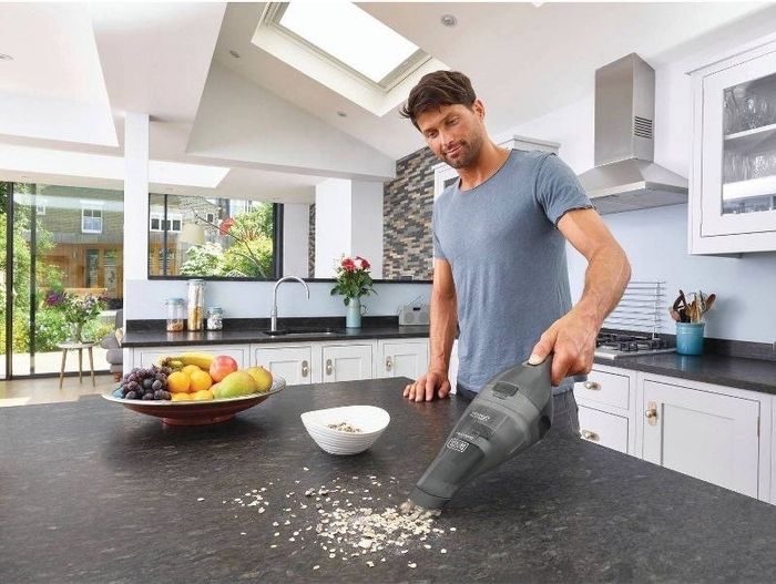 A person uses a handheld vacuum to clean up crumbs.