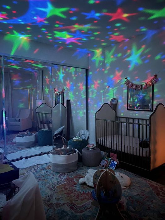 A nursery featuring a crib, toys, and a light projector casting celestial patterns on the walls and ceiling