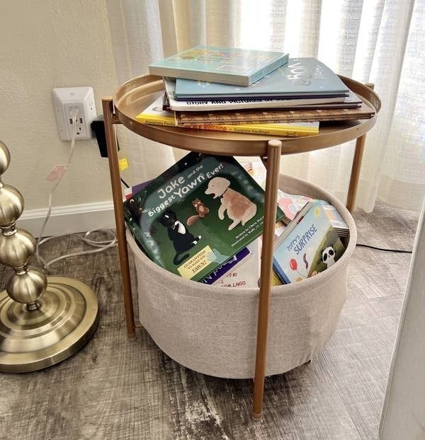 A circular side table featuring a storage compartment, adorned with books, serving as both functional and decorative home furniture