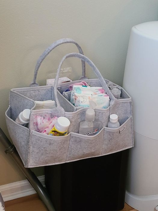 A gray storage caddy with compartments holding baby supplies like wipes and lotions, placed near a diaper pail. Ideal for nursery organization