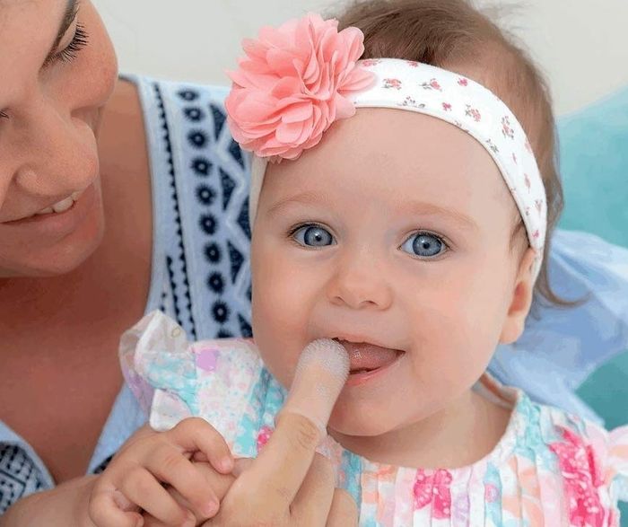 A woman and her baby, who is wearing a headband, using a finger tool to clean the baby's teeth