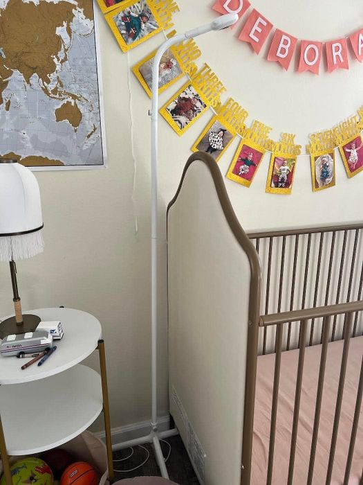 A cozy bedroom featuring a banner, floor lamp, and side table beside a crib, with decorative accents creating a personalized atmosphere