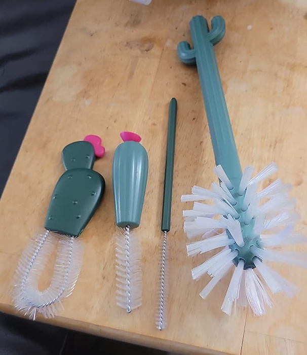 A collection of four green and white cleaning brushes for bottles and straws, featuring cactus and flower designs, neatly arranged on a wooden surface