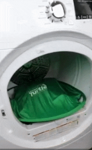 A person using a green, flexible net device with outer rods to efficiently scoop clothes out of the dryer
