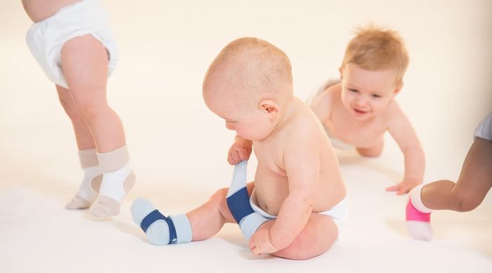 Three infants in diapers and baby socks, with two crawling and one sitting