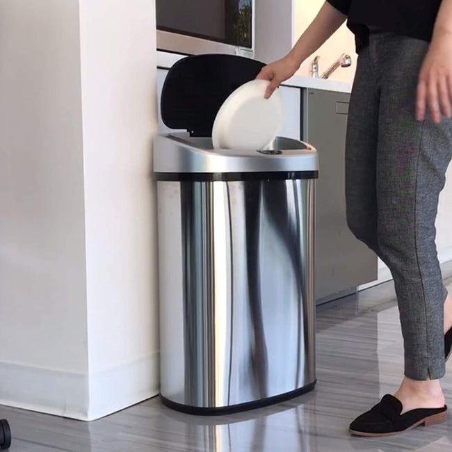 A model tossing trash into a stainless steel trash can with its lid automatically opening