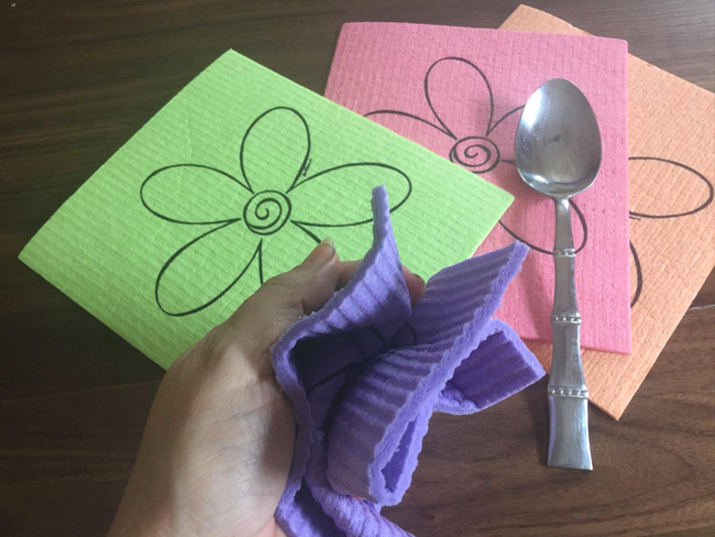 Reviewer wringing out a purple towel beside a set of green, pink, and orange towels on a table