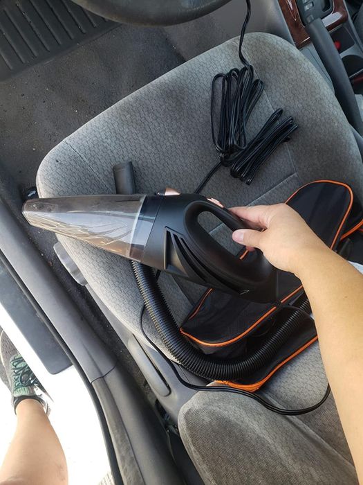 reviewer holding a black portable car vacuum above a car seat