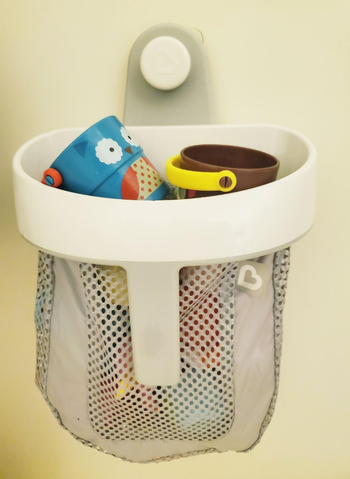 A gray mesh bag filled with toys, hanging on a shower wall