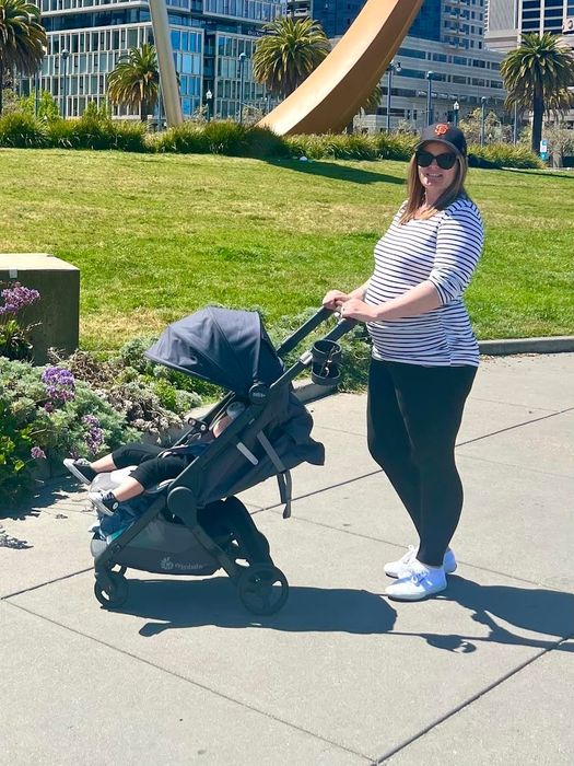 A woman dressed in a striped top, leggings, and sneakers, pushing a stroller, ideal for outdoor family outings or shopping