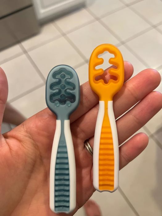 Two silicone teething spoons with unique patterns, being held in a hand