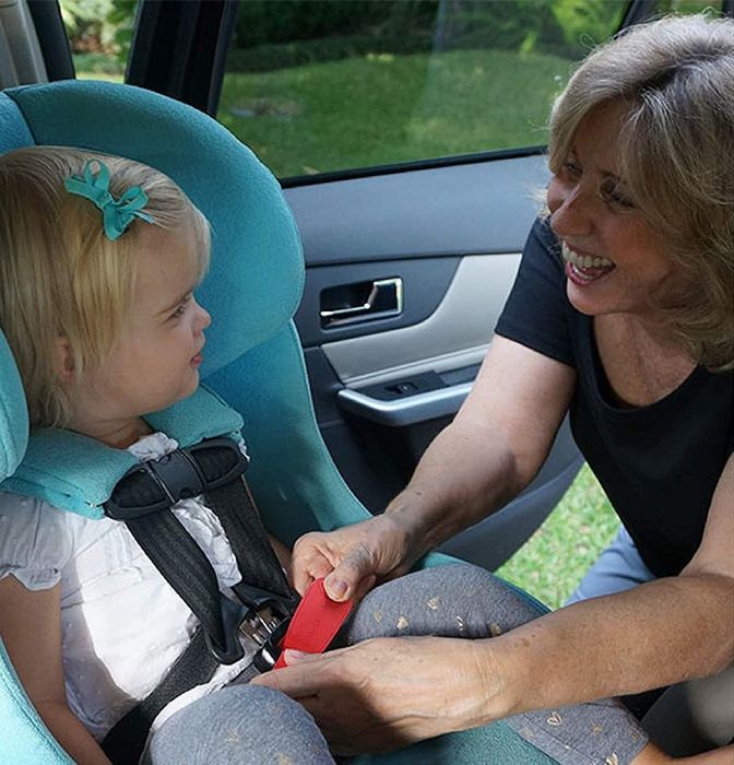 An adult ensuring a child is safely secured in a car seat