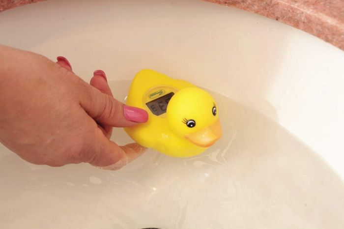 A hand holding a yellow rubber duck equipped with a built-in thermometer, ideal for checking bath water temperature