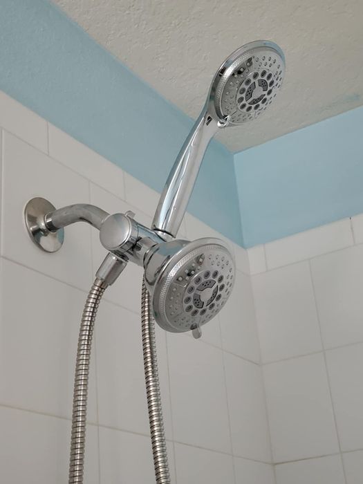 A bathroom featuring dual showerheads mounted on the wall, one fixed and one handheld, in a beautifully tiled shower area.