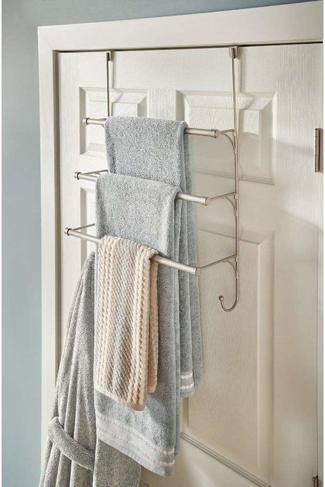 The back of a bathroom door featuring a towel rack with three tiers for towels