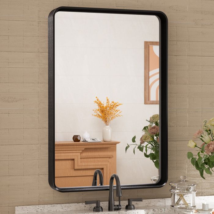 A wall mirror reflecting a bathroom vanity, decorated with a vase of yellow flowers and various bathroom accessories.