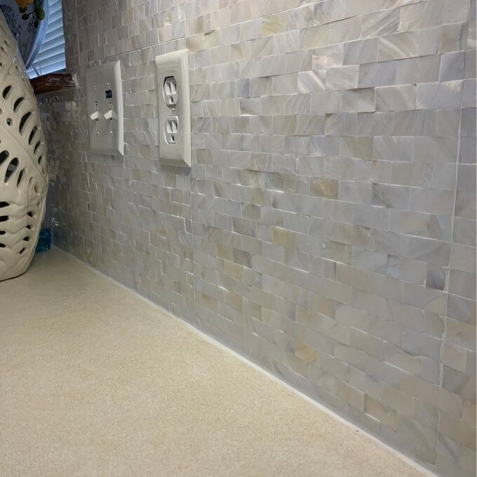 The mother of pearl tiles adorning a wall around an electrical outlet.