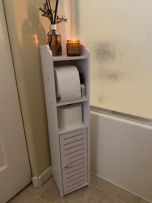A white bathroom caddy with rolls of toilet paper and a lit candle placed on top