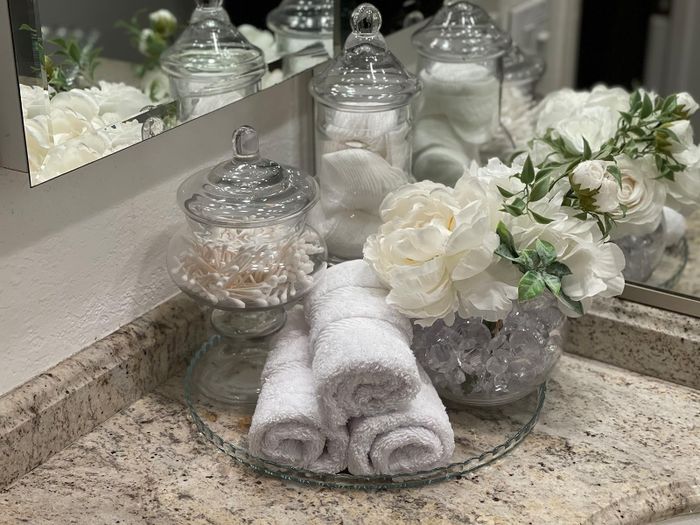 A bathroom vanity featuring jars of cotton products, rolled towels, and decorative flowers