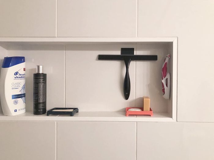 A shelf with personal care items, including a squeegee, a bottle, a razor, and soap.