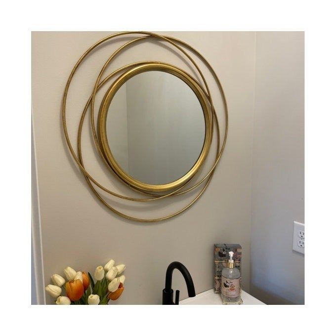 A round, gold-framed mirror hanging above a sink.