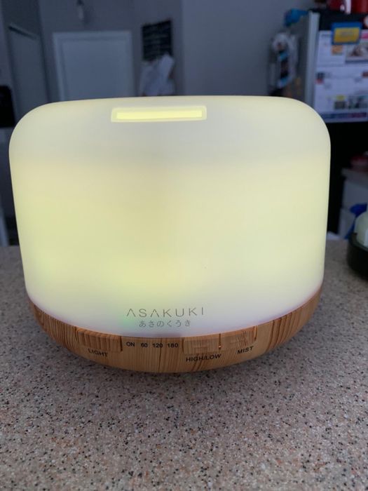 An essential oil diffuser featuring a glowing top and a wooden base, placed on a bathroom counter.
