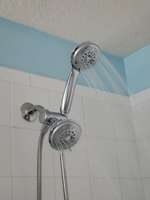 A pair of showerheads installed on a bathroom wall, with water flowing from one of them.