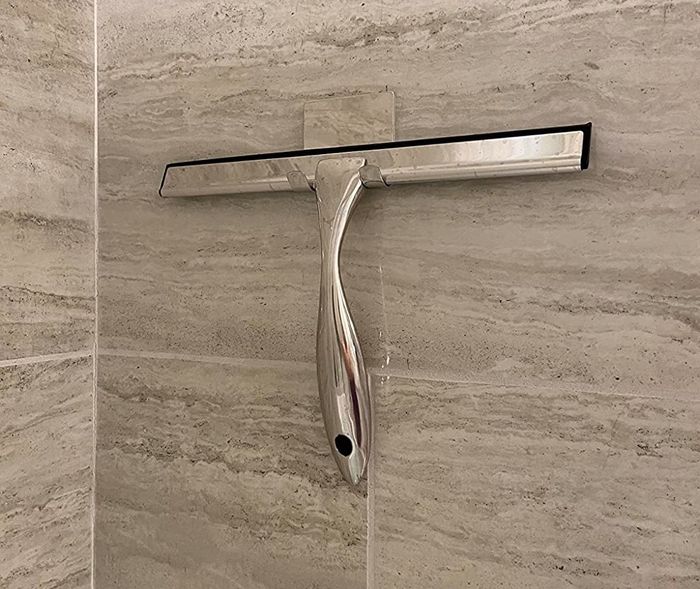 A squeegee hanging on a tiled wall.