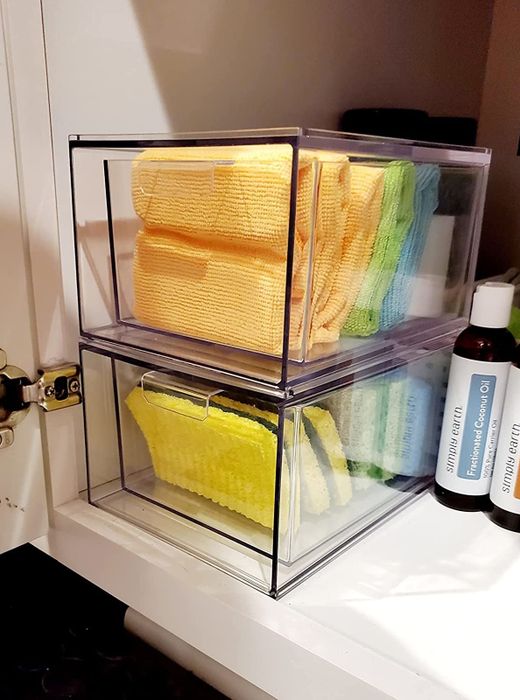 Two clear storage boxes stacked on a shelf, holding towels and sponges next to toiletries, making use of vertical space for organization.