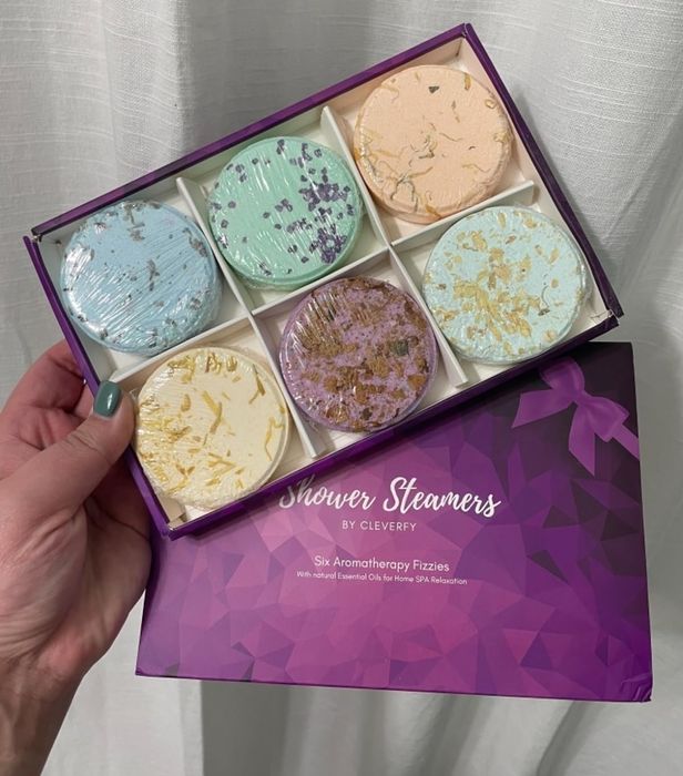 A hand holding a box of six shower steamers, labeled 'Shower Steamers by Clevery,' showcasing a variety of textures.