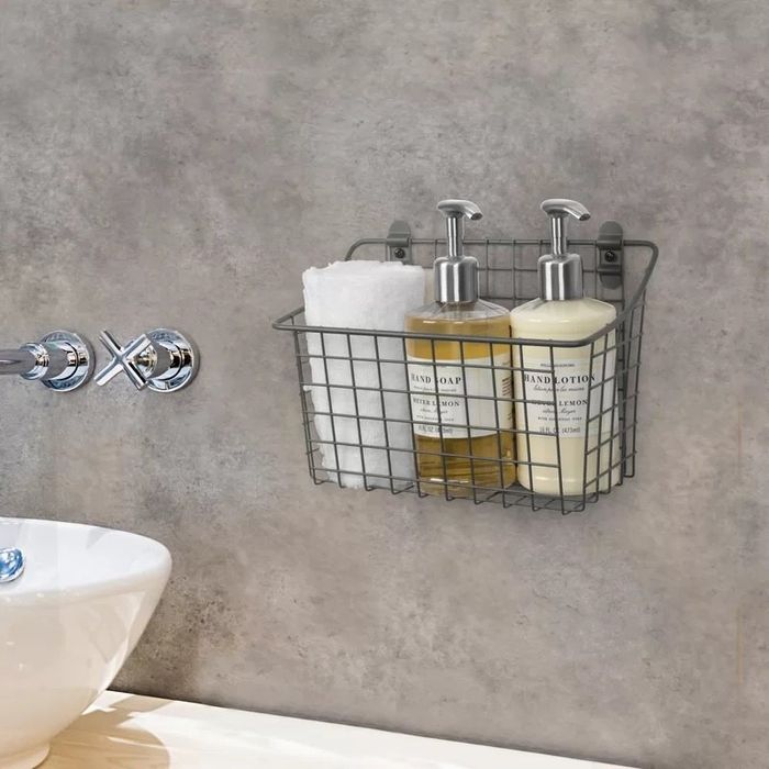 A metal wire shower caddy mounted on a bathroom wall holds two soap dispensers and a neatly folded washcloth.