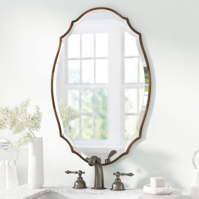 A beautifully designed wall mirror with a distinctive frame, elegantly positioned above a bathroom sink.