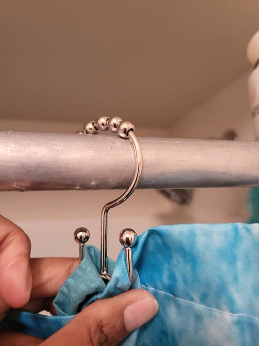 A reviewer's photo showcasing the silver hooks, demonstrating how the curtain and liner are attached on separate sides.