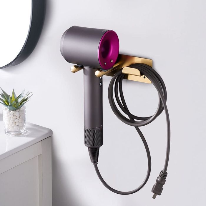 A Dyson hair dryer with attachments mounted on the wall, set against a backdrop of a small plant and mirror, adding both functionality and style to your bathroom.