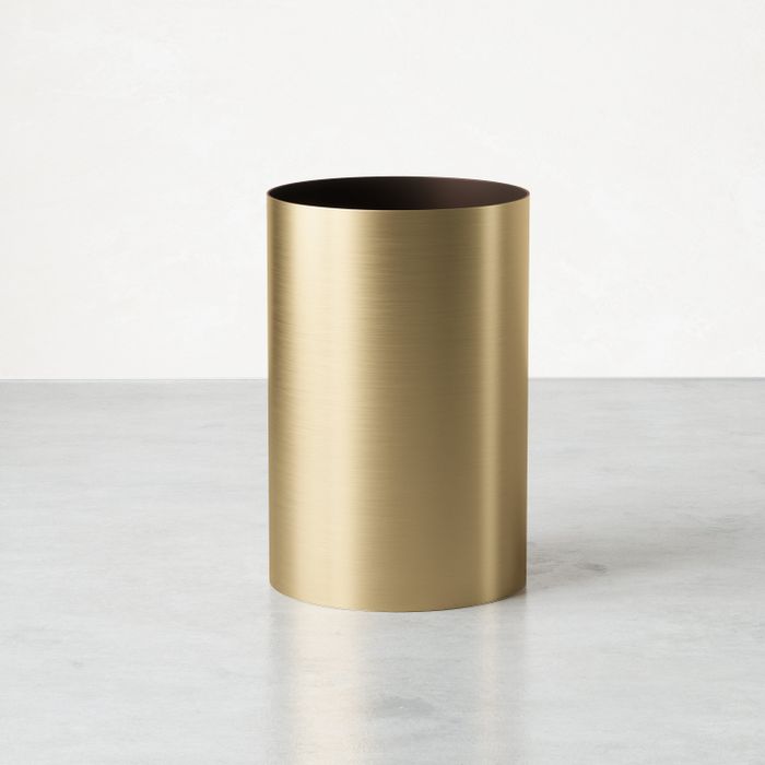 A cylindrical wastebasket with a brushed brass appearance.